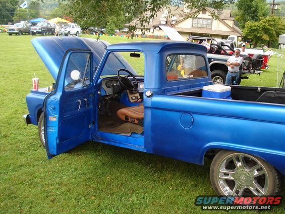 Blue pickup truck with hood and door open, showing interior. Other trucks in background