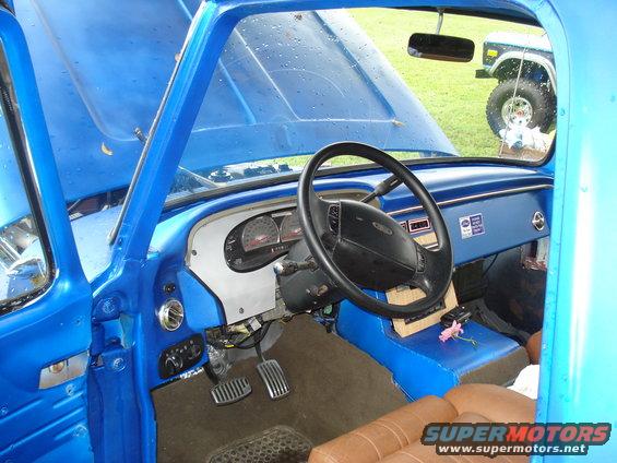 Blue 1992 Ford F-150 interior with tan seats and aftermarket gauges. A pink flower rests on the center console