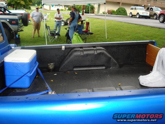Blue pickup truck bed with a blue cooler and a white tarp
