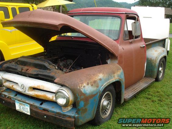 Rusty 1953 Ford F-100 pickup truck, hood open, parked next to a yellow van