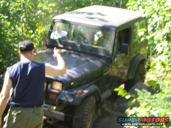 Dark Jeep Wrangler on wooded trail, driver giving thumbs up