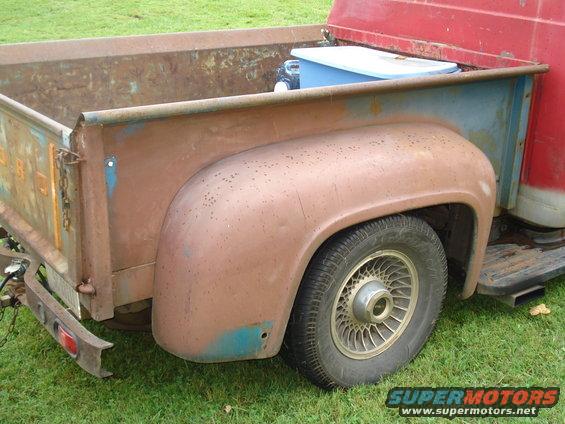 Close-up of a rusty pickup truck's rear fender and bed, showing a blue cooler inside