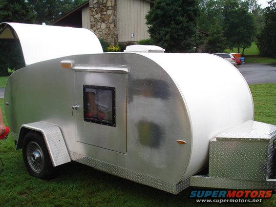Teardrop trailer with a white curved roof and a silver body. It has one door with a small window