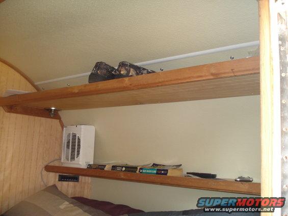Interior shelves in a camper with shoes on the top shelf and books and a fan on the lower shelf