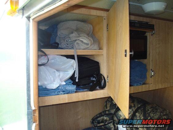Interior view of open wooden cabinets filled with clothes and bags. A microwave is visible in a separate compartment