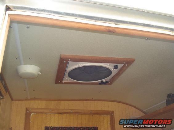 RV interior ceiling with vent and light fixture. Wood trim visible