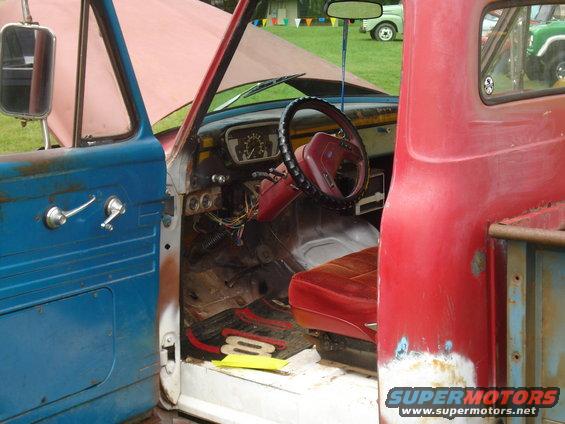 Interior of an old pickup truck with a blue door and red seat. Hood is up