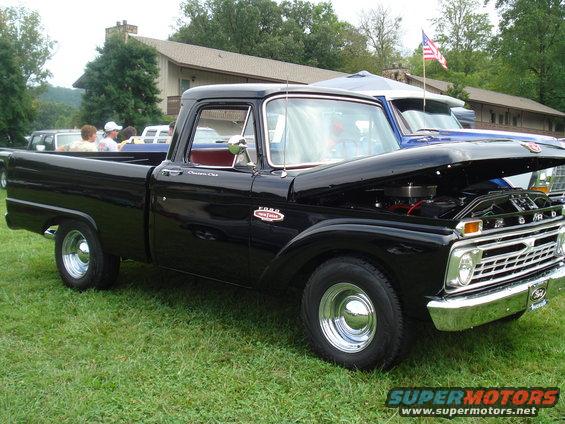 Black Ford pickup truck, hood open, parked on grass. Another vehicle is partially visible behind it