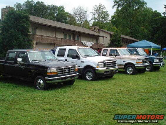 Four Ford F-Series trucks parked on grass in front of a building. The trucks appear to be from the late 90s