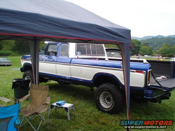 Side view of a blue and white 1970s Ford pickup truck parked under a canopy