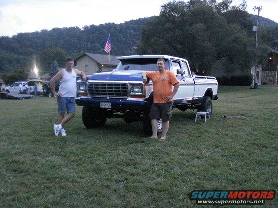 Blue and white Ford F-Series truck with two men standing next to it. The truck has a lifted suspension and large tires
