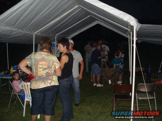 People stand around talking under a large white tent at night