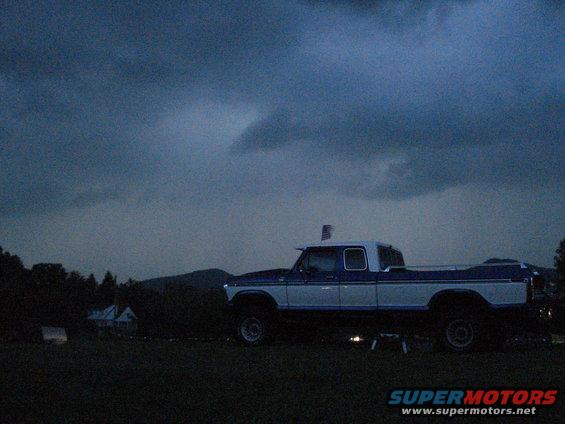 Blue and white pickup truck parked in a field under a cloudy sky