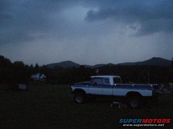 Blue and white pickup truck parked in a grassy field with hills in the background