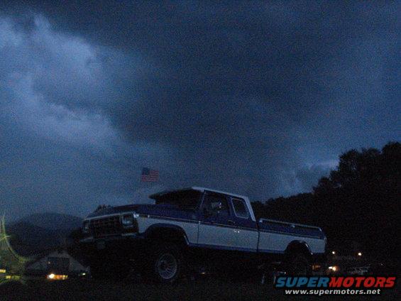 Ford F-Series pickup truck with blue and white two-tone paint, lifted suspension, under a dark, cloudy sky