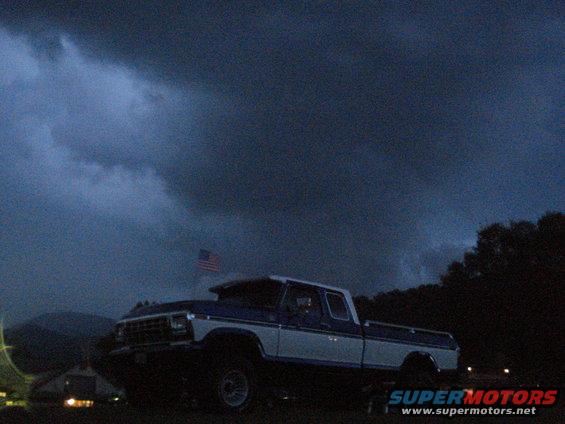 Pickup truck with an American flag in the background under a stormy sky