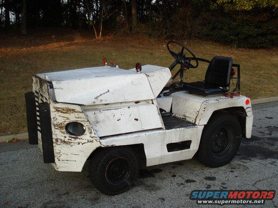White tow tractor with black grille and black seat, showing dents and rust