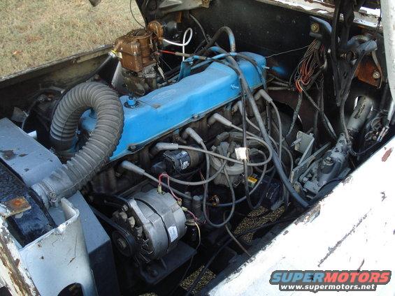 Engine bay with blue valve covers, carburetor, and alternator. White exterior visible
