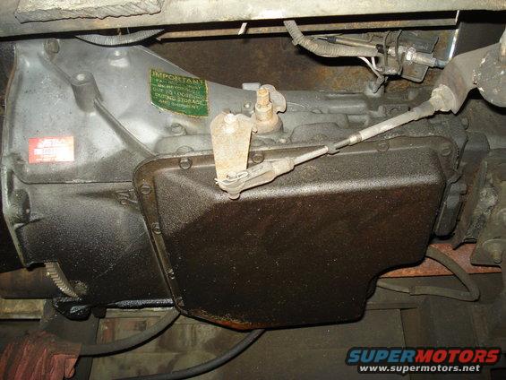 Transmission pan with a green 'IMPORTANT' sticker and a red sticker. Oily residue covers the metal