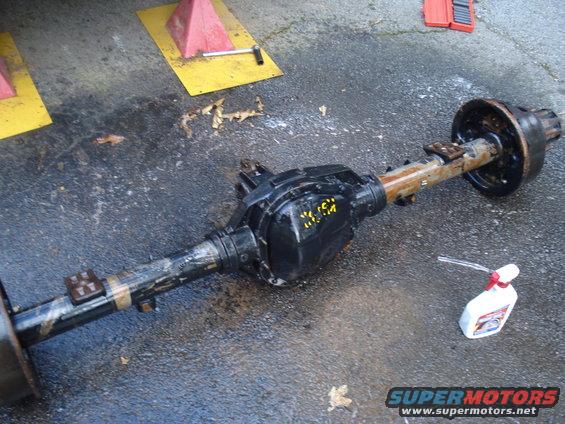 Rear axle assembly with yellow markings on the differential cover, sitting on asphalt