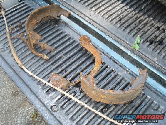 Rusted brake shoes, wheel cylinder, and parking brake cable laid out on a truck bed