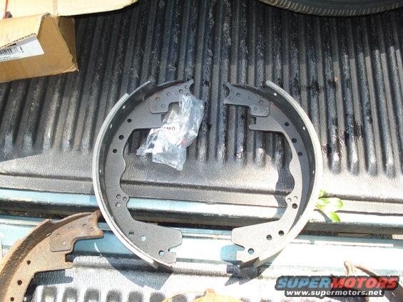 New brake shoes in plastic packaging next to old, rusty brake shoes on a truck bed