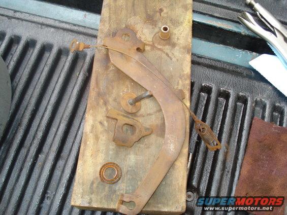 Rusty brake pedal lever, spring, and mounting bracket on a piece of wood