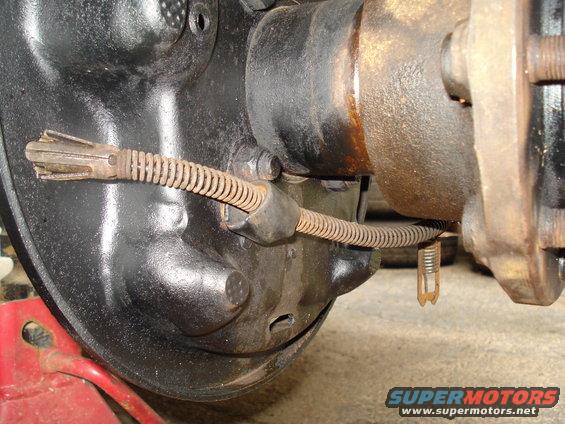 Close-up of a vehicle's rear brake drum and parking brake cable assembly