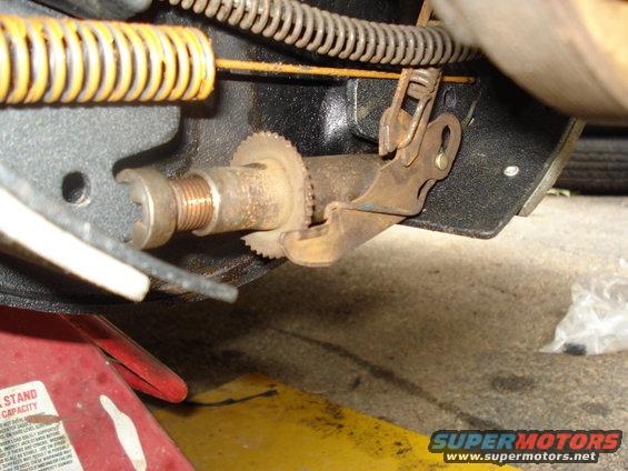 Close-up of a rusty parking brake mechanism with a yellow spring and a red jack stand