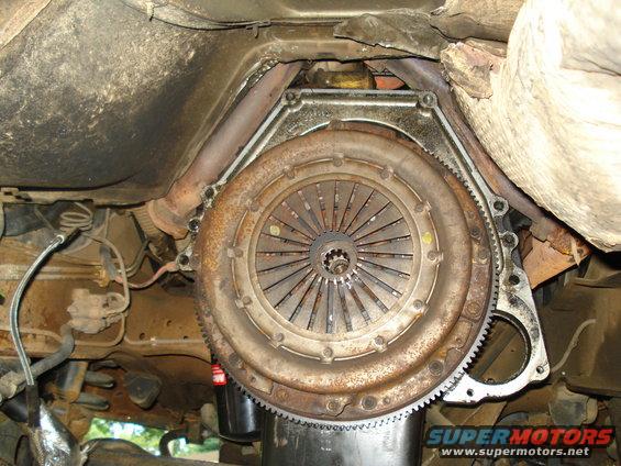 Underside view of a vehicle's clutch and transmission assembly. Shows the flywheel and pressure plate