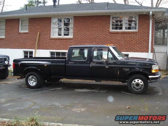 Black crew cab dually pickup truck parked on asphalt, side view. Visible front fender badge reads "F-350"