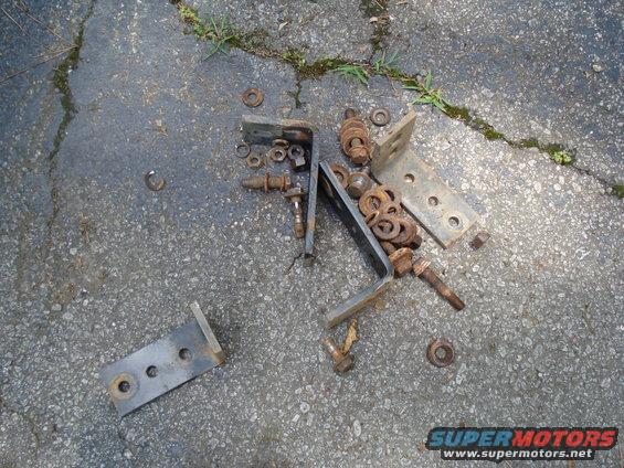 Pile of rusty metal brackets, bolts, and washers on asphalt