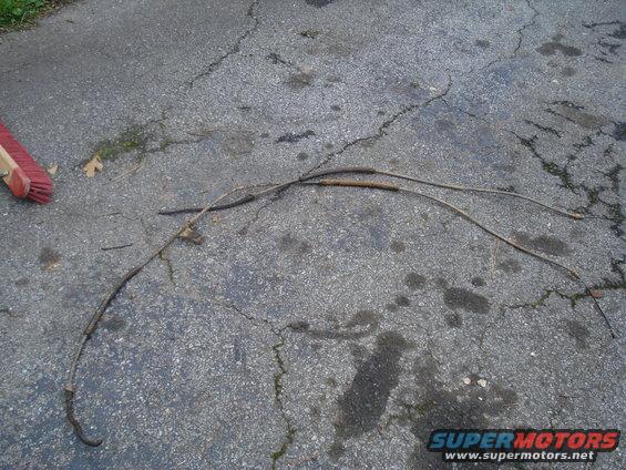 Two brake cables lying on cracked asphalt, with a red-bristled broom head visible on the left