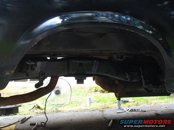 Black truck frame and wheel well, showing rusty exhaust pipe and fan. The vehicle is on jack stands