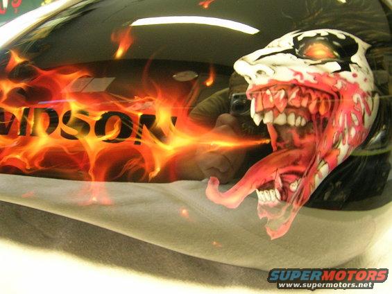 Motorcycle gas tank with flames and a monster face airbrushed on it. Text reads "HARLEY-DAVIDSON"