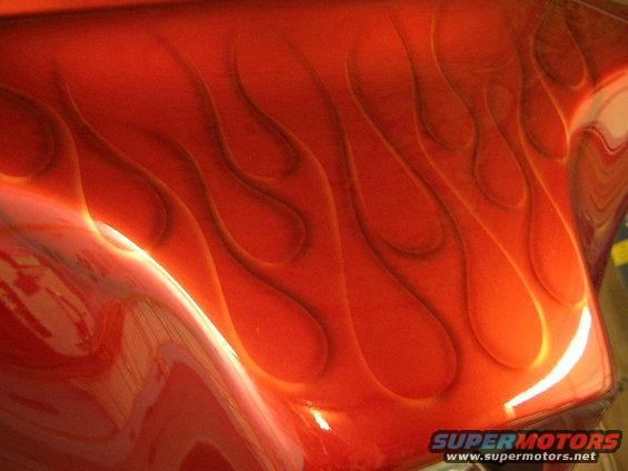Close-up of red vehicle part with airbrushed flame graphics. Watermark at bottom right