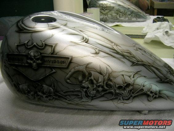 Motorcycle gas tank with airbrushed skulls and flames, silver and black crackle paint. 'Harley Davidson' badge visible
