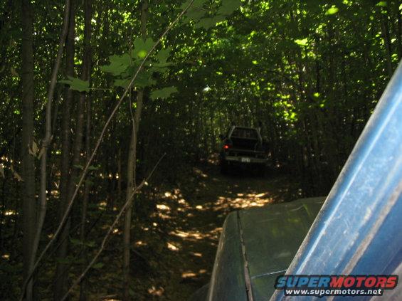 View from inside a vehicle looking out at another truck on a dirt trail in a forest