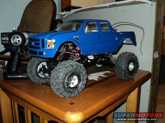 Blue RC monster truck with large tires and a remote control. Looks like a Ford F-250 body