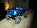 2008 Ford F-250 - This RC monster truck, resembling a 2008 Ford F-250, features oversized tires and a bright blue body, perched on a textured couch.