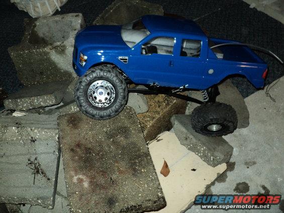 Blue 2008 Ford F-250 RC truck on concrete blocks, front 3/4 view