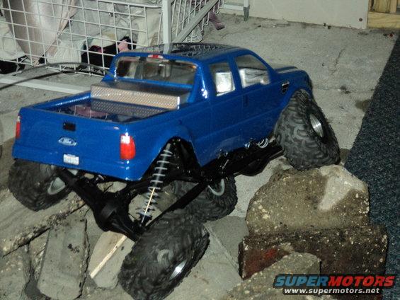 Blue RC truck with large tires on rocks. Diamond plate toolbox in bed