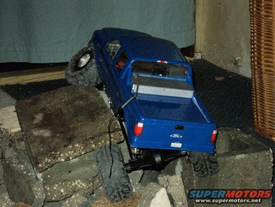 Blue RC truck with large tires climbing over concrete blocks. Ford logo visible on tailgate