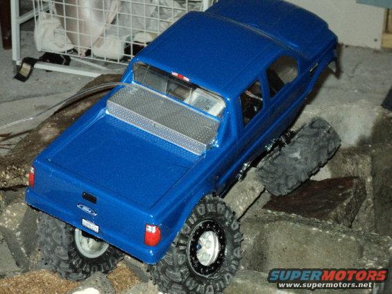 Blue RC pickup truck with large tires climbing over rocks