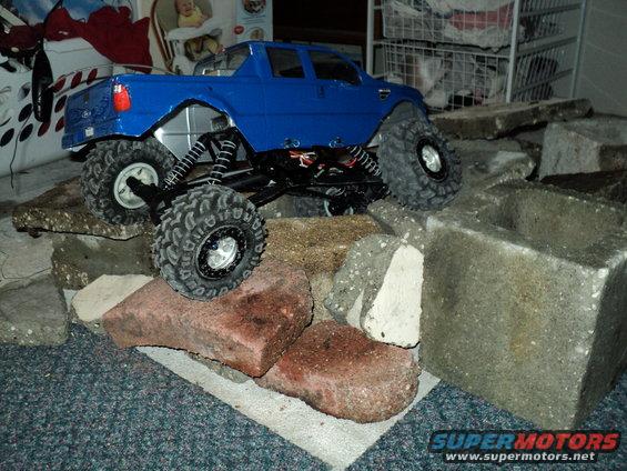 Blue RC rock crawler truck with large tires on bricks and concrete blocks