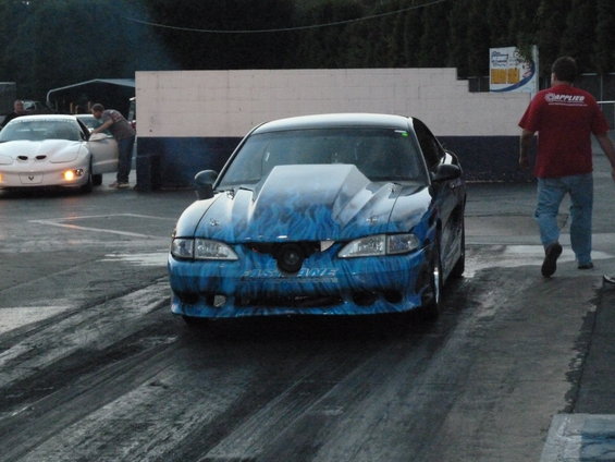 Blue drag car with flame graphics and a large hood scoop, angled from the front