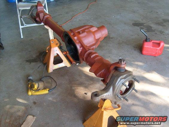 Front axle assembly on jack stands, with a red jerry can and yellow power tool nearby