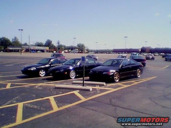 Several dark-colored cars parked in a lot on a sunny day