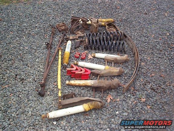 Assorted suspension parts including shocks, springs, and linkages on a gravel surface