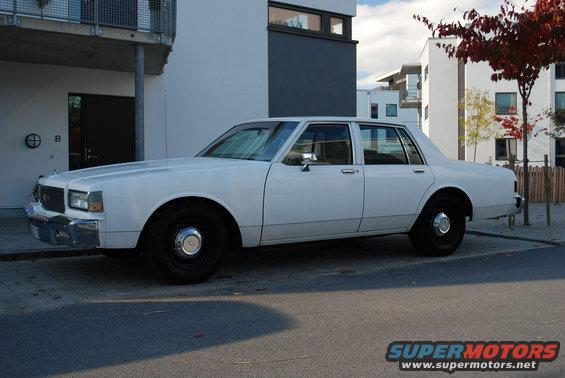 White 1980s sedan parked on street, side view